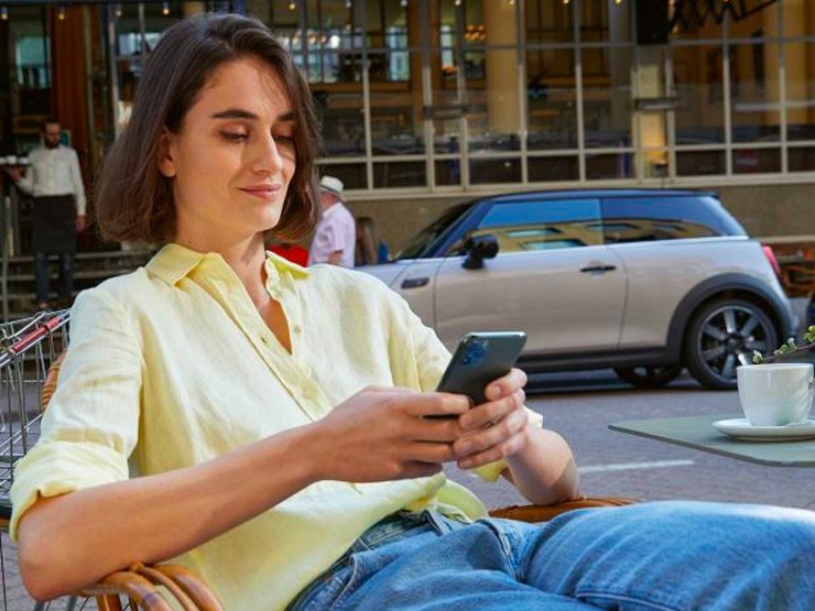 Vrouw kijkt op haar telefoon met een MINI op de achtergrond.